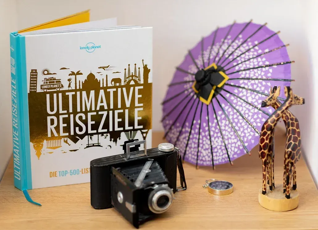Ein Buch mit dem Titel „Ultimative Reiseziele“ liegt neben einer Kamera und einem Regenschirm