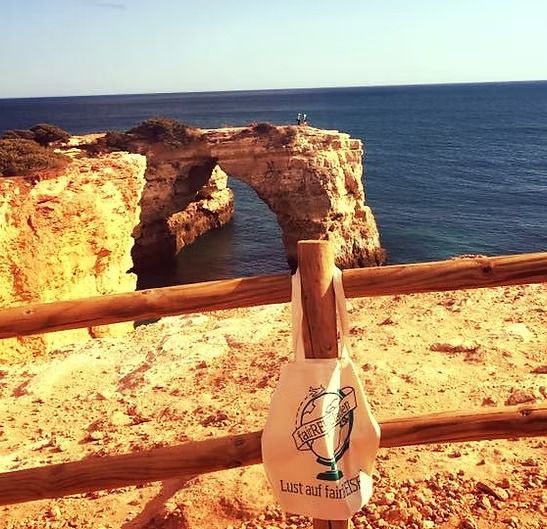 Eine Tasche mit einem Fisch darauf hängt an einem Holzzaun mit Blick auf den Ozean