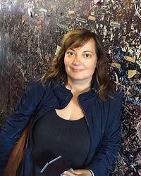 Eine Frau in einer blauen Jacke steht vor einer Wand mit Graffiti.