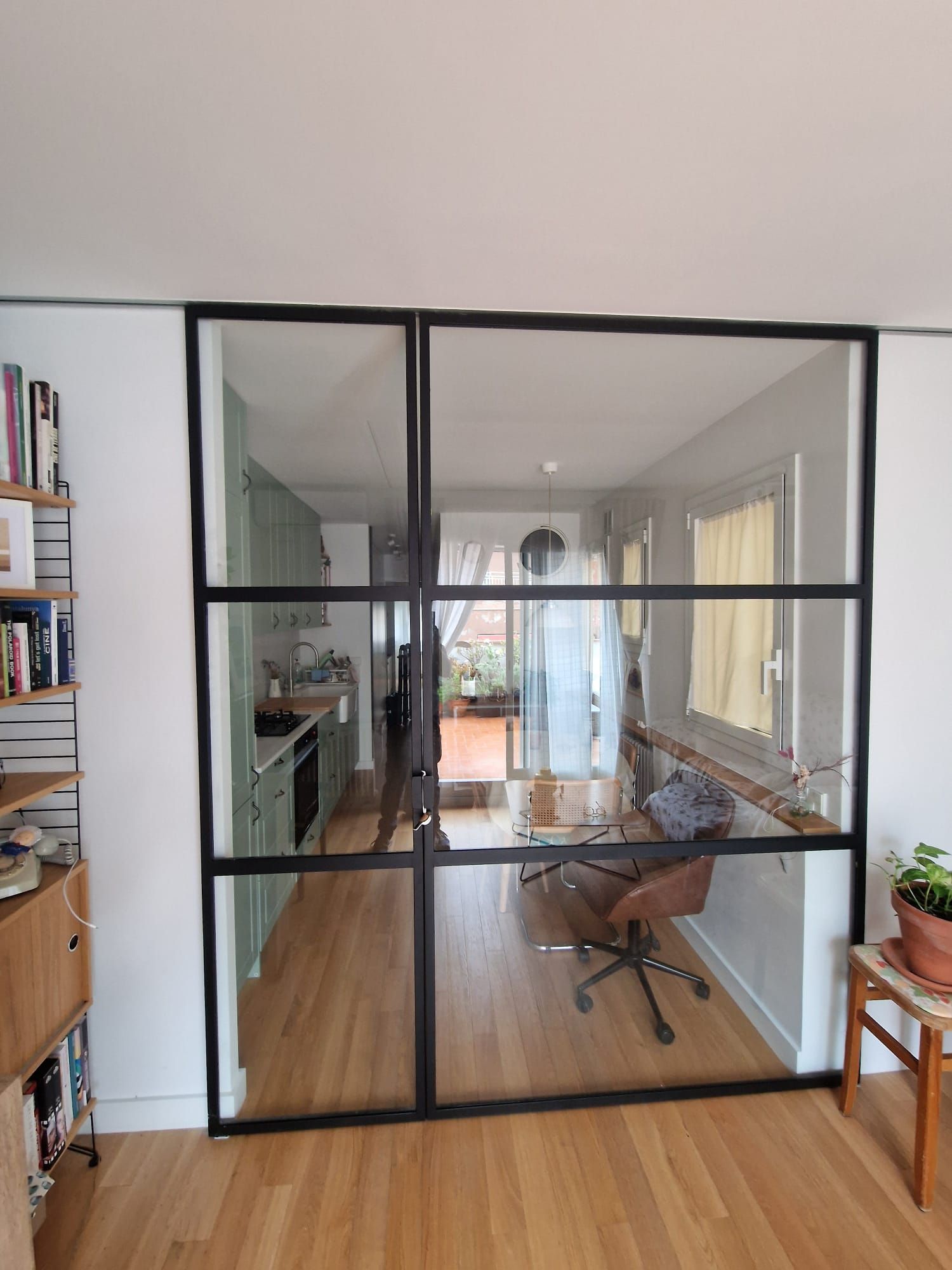 Oficina moderna en casa con mampara de cristal con marco negro, escritorio, silla y suelo de madera