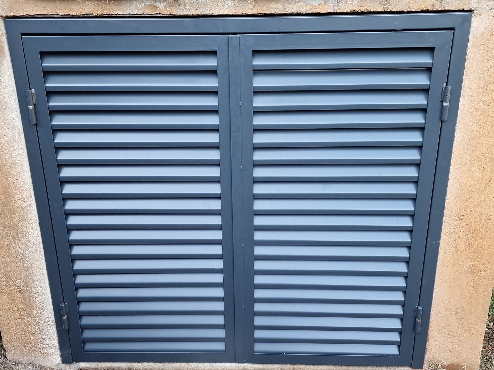 Contraventanas azules de metal con lamas, instaladas en una pared beige