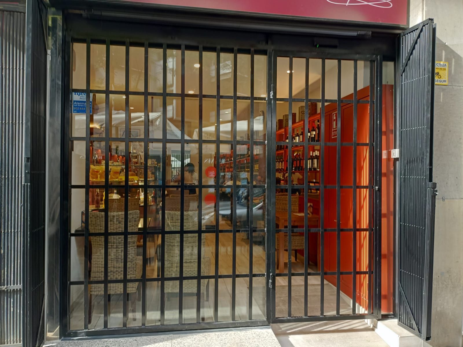 Tienda cerrada con rejas de seguridad negras y una puerta roja en el interior de la entrada de un centro comercial