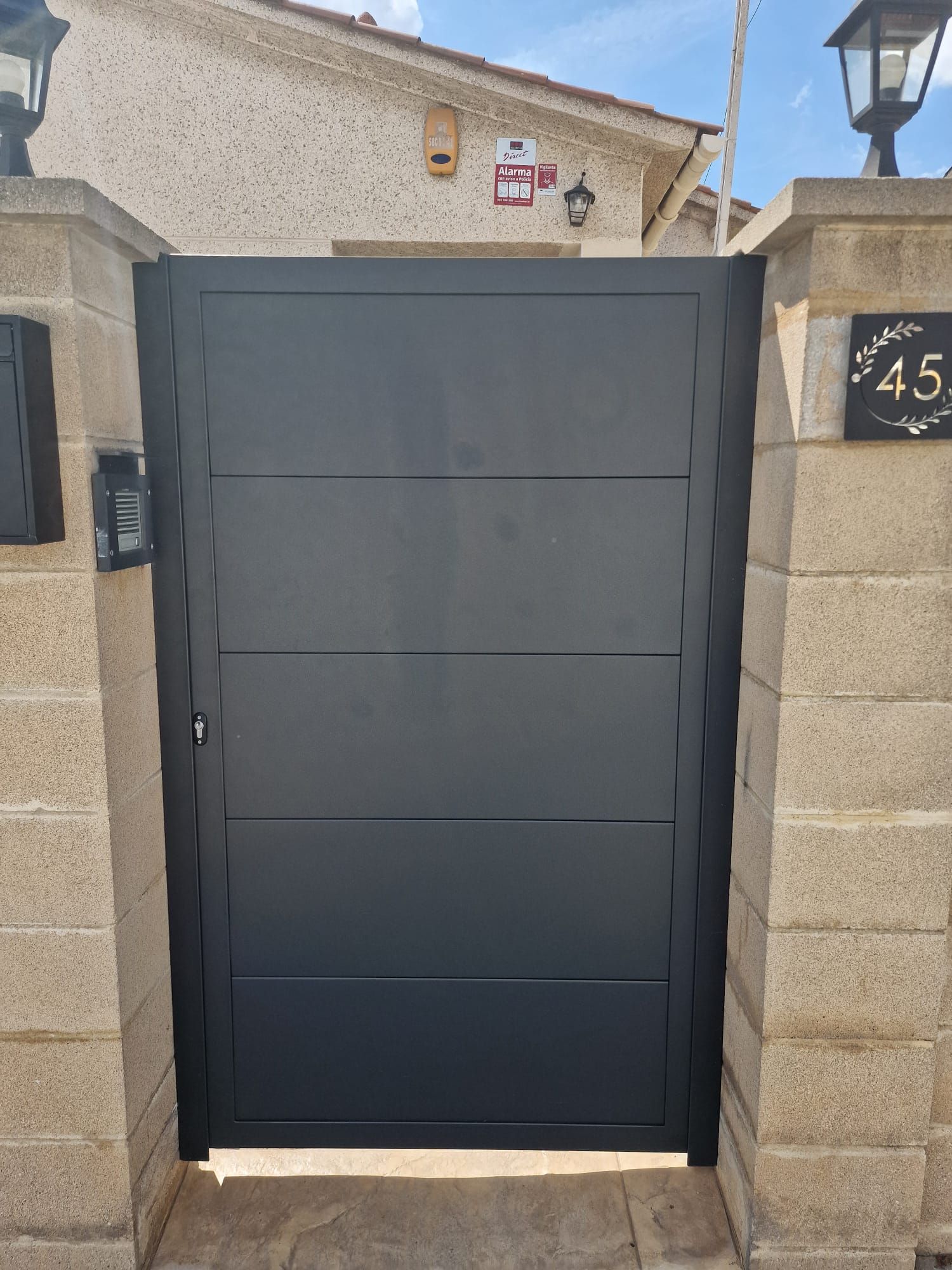 Portón metálico gris oscuro en un muro de piedra a la entrada de una vivienda