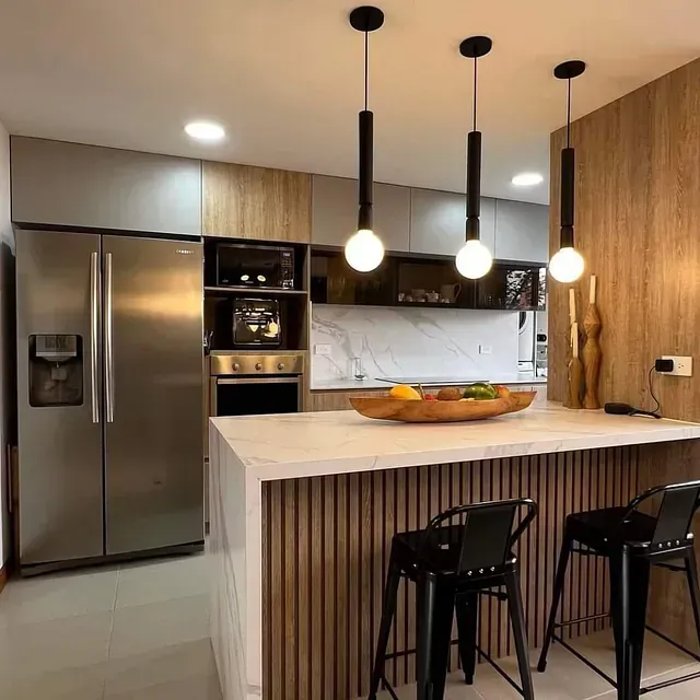 Una cocina con taburetes, un refrigerador, un fregadero y una mesa con un recipiente con comida encima.