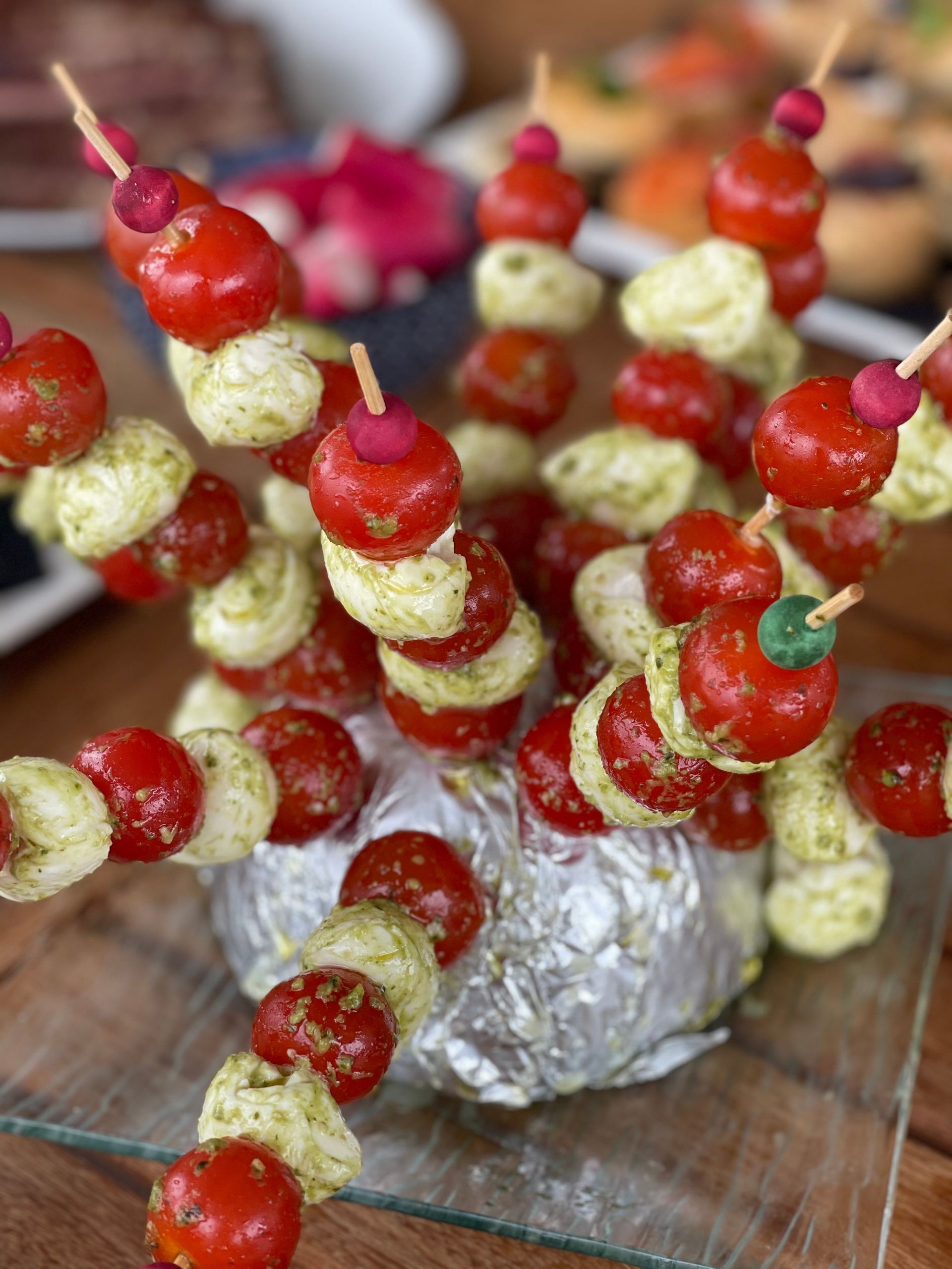 Brochettes Caprese : tomates cerises, boules de mozzarella au pesto et radis sur brochettes, disposées sur du papier aluminium.