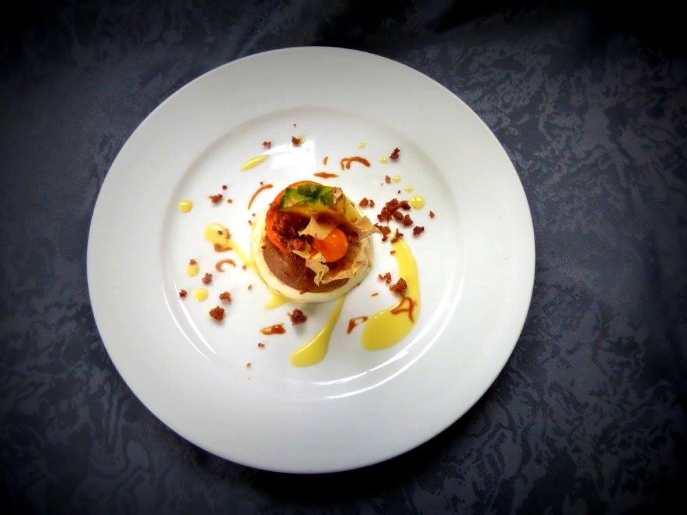 Une assiette blanche présentant un plat gastronomique composé d'un œuf au plat, de sauce et de garniture.