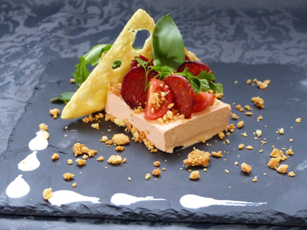 Entrée restaurant Une entrée composée de pâté aux tomates, aux herbes et d'une tuile de fromage, présentée sur une assiette en ardoise.
