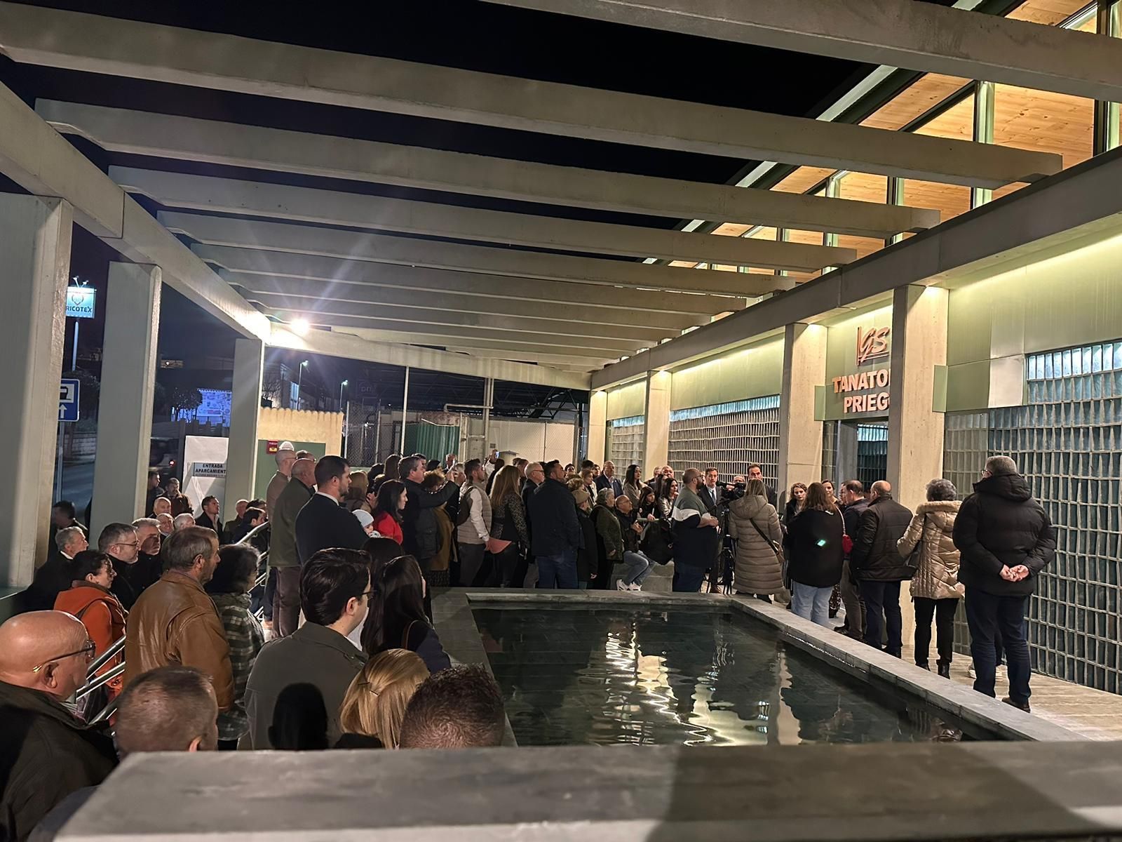 Un grupo de personas están de pie alrededor de una piscina por la noche.