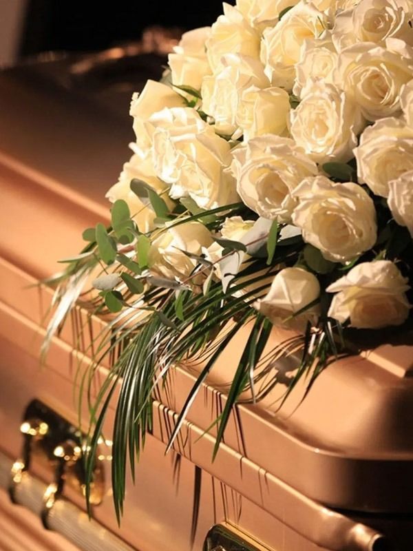 Un ataúd está decorado con rosas blancas y vegetación.