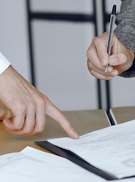 Una persona sostiene un bolígrafo y señala un trozo de papel.