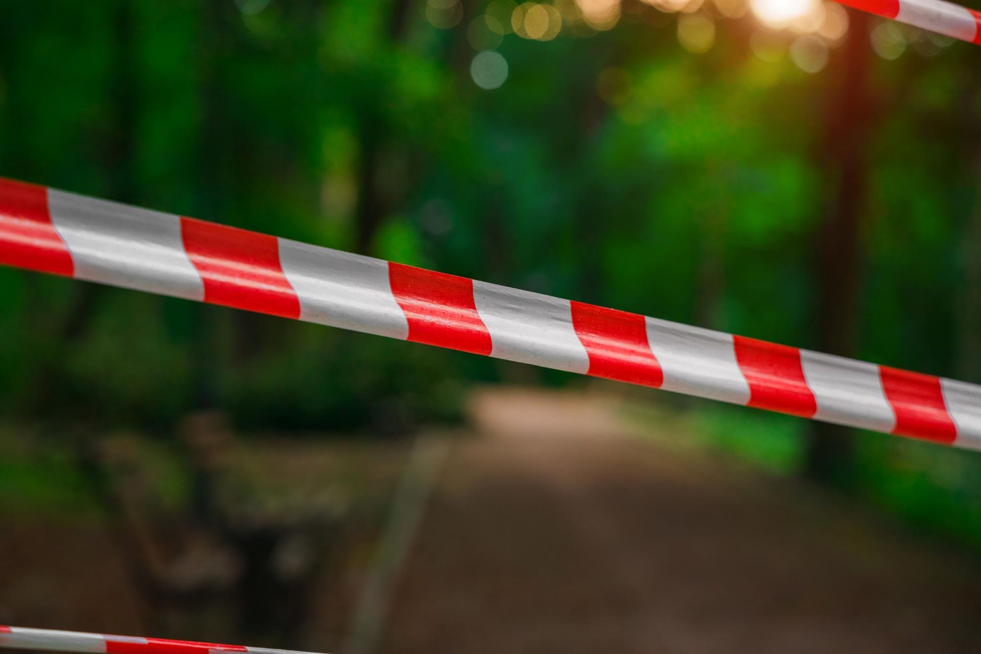 Una cinta de precaución con rayas rojas y blancas bloquea un camino borroso en un parque.