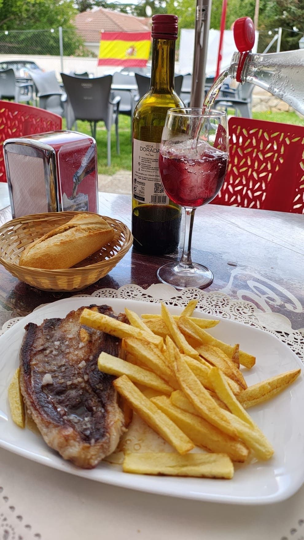 Un plato de comida con patatas fritas y una botella de vino en una mesa.