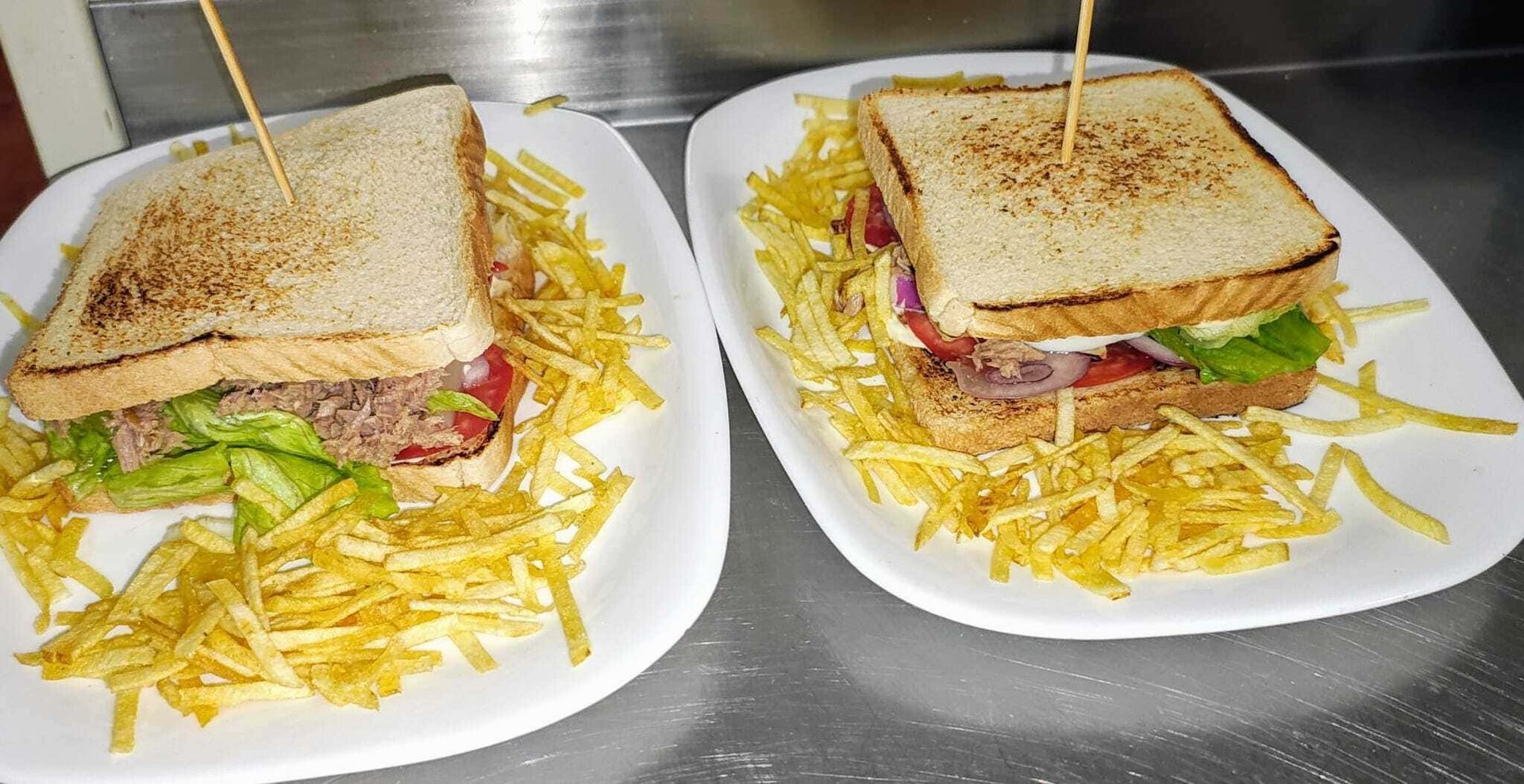 Dos sándwiches en platos blancos con papas fritas encima