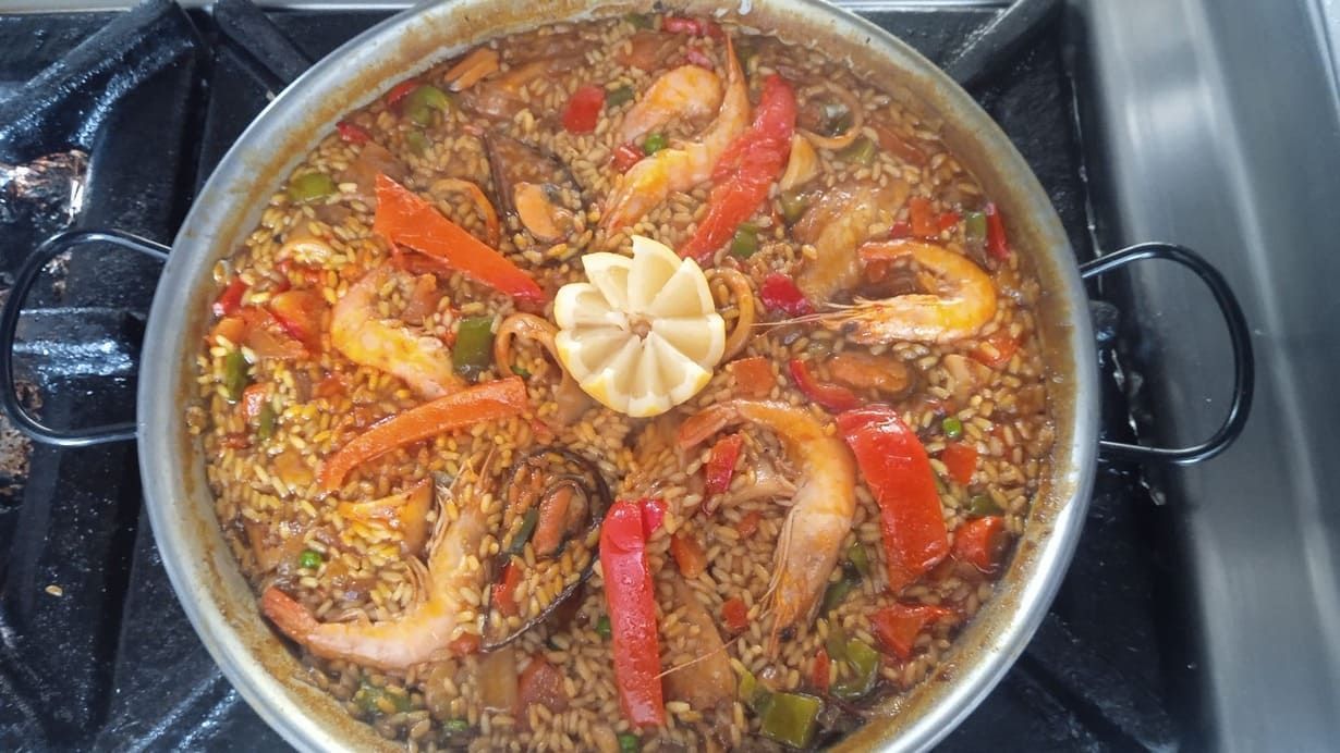Una sartén de paella con camarones y verduras al fuego.