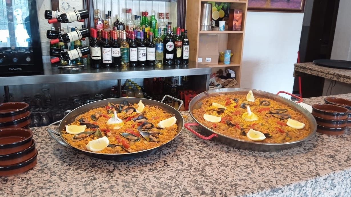 Hay dos sartenes de paella sobre un mostrador delante de una barra.