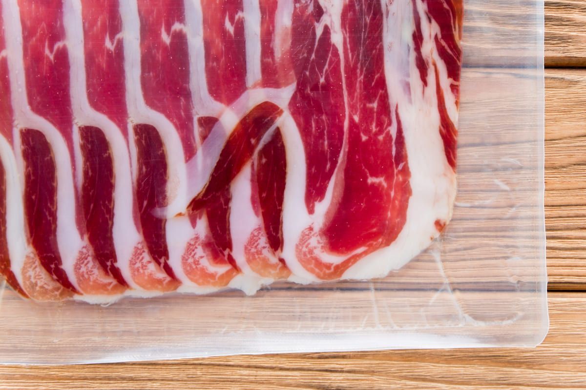 Un primer plano de un trozo de tocino envuelto en plástico sobre una mesa de madera.