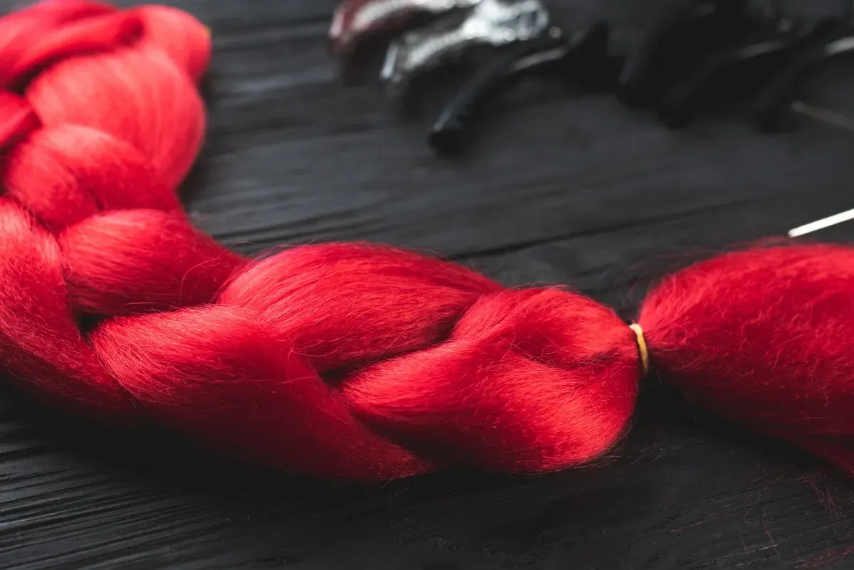 Persona con trenzas africanas color burdeos, se extienden hasta formar una cola de caballo.