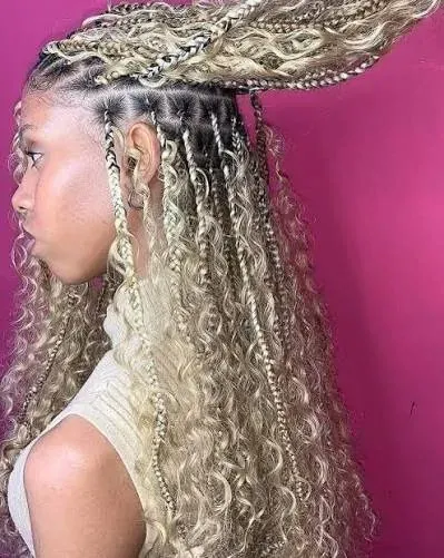 Mujer con trenzas rubias y extensiones rizadas, vista de perfil sobre fondo rosa.