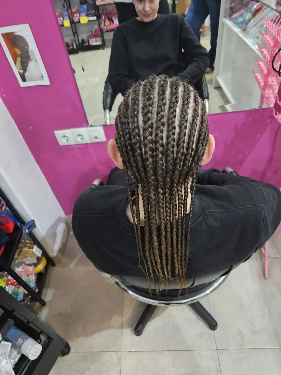 Persona con cabello largo y trenzado sentada en una silla de salón. Las trenzas son oscuras con puntas claras.