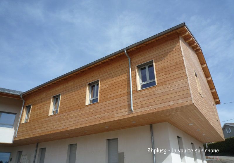 Bâtiment avec bardage en bois et partie inférieure blanche, ciel bleu.