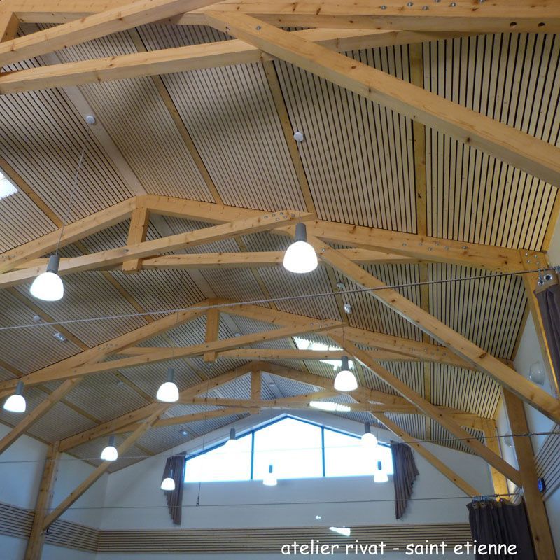 Plafond à charpente apparente en bois avec luminaires suspendus, puits de lumière incliné et toiture à panneaux.