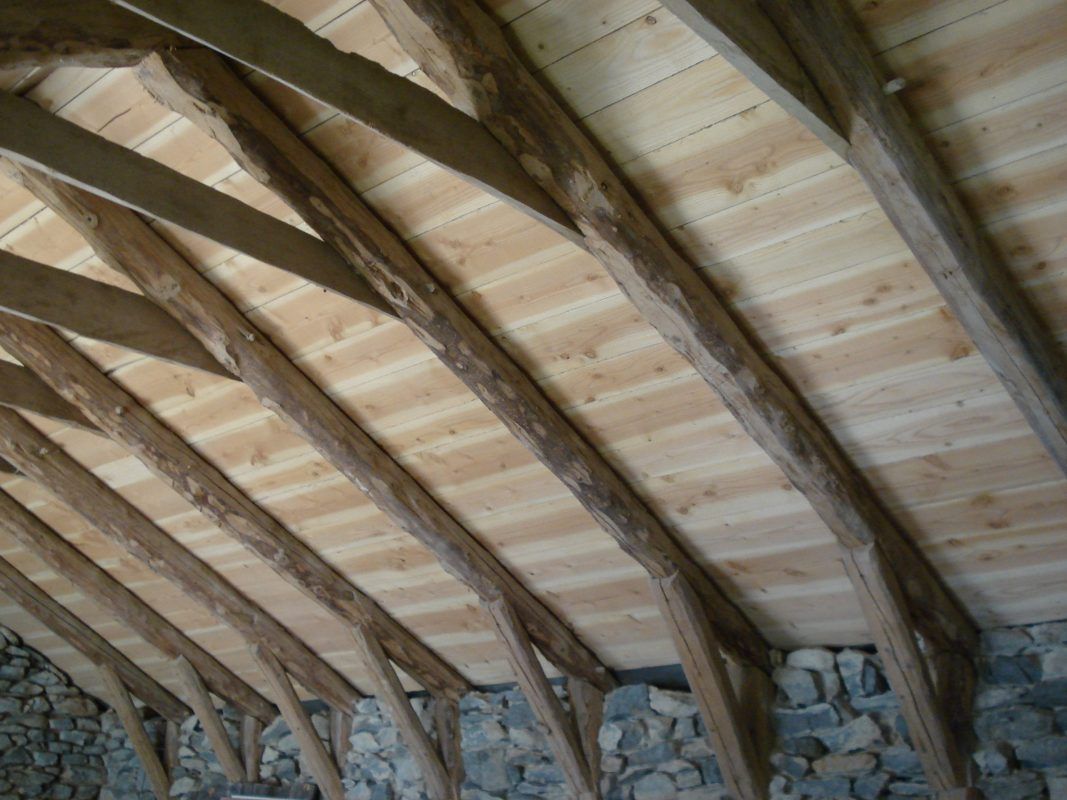 Poutres de toit en bois et lambris clair sur un plafond en pierre.
