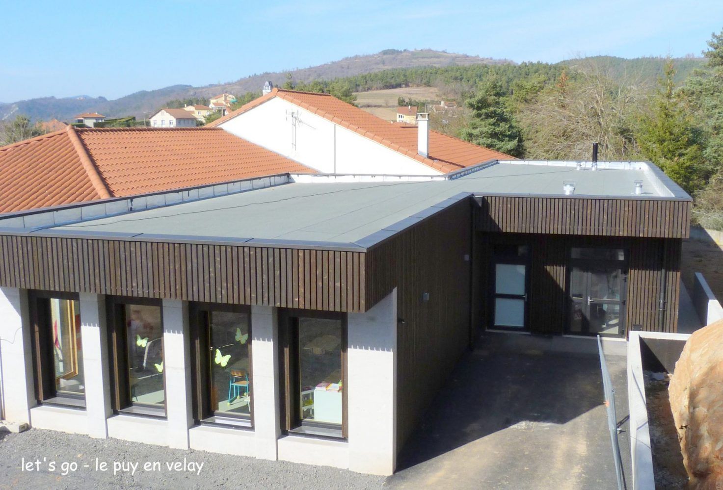 Bâtiment avec un toit de tuiles rouges et un toit plat gris, un bardage en bois brun et des fenêtres.