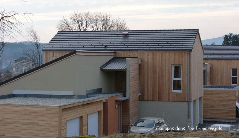 Bâtiments modernes revêtus de bois, avec des toits en pente et des tuiles grises, se détachant sur un ciel nuageux.