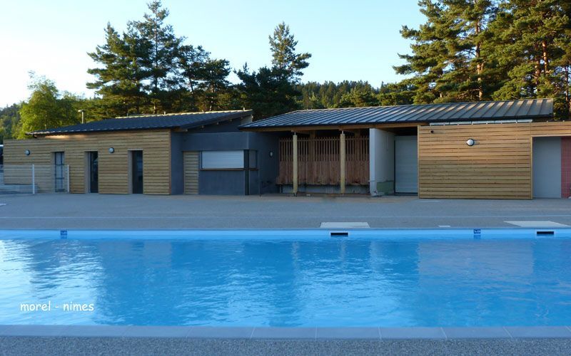 Piscine à l'eau bleue devant un bâtiment à bardage en bois et toit gris, entourée d'arbres.