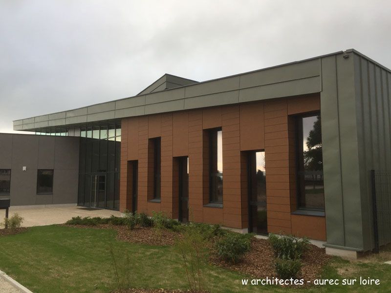 Bâtiment moderne avec une façade brune et grise, de hautes fenêtres et une pelouse.