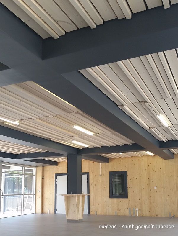 Vue intérieure d'une pièce avec plafond à lattes de bois, poutres sombres et murs lambrissés.