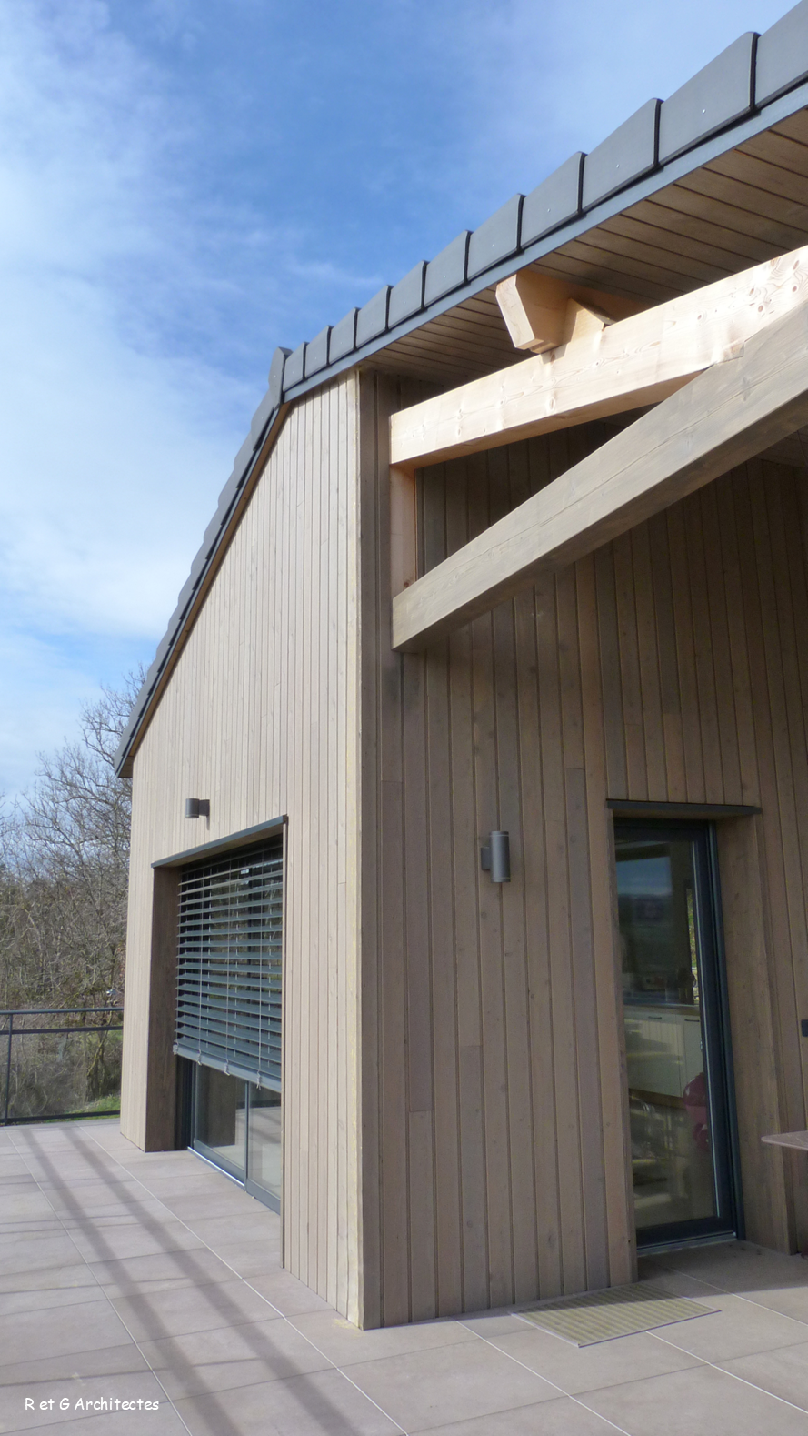 Extérieur d'un bâtiment en bois avec bardage vertical, fenêtre et porte sous un ciel bleu.