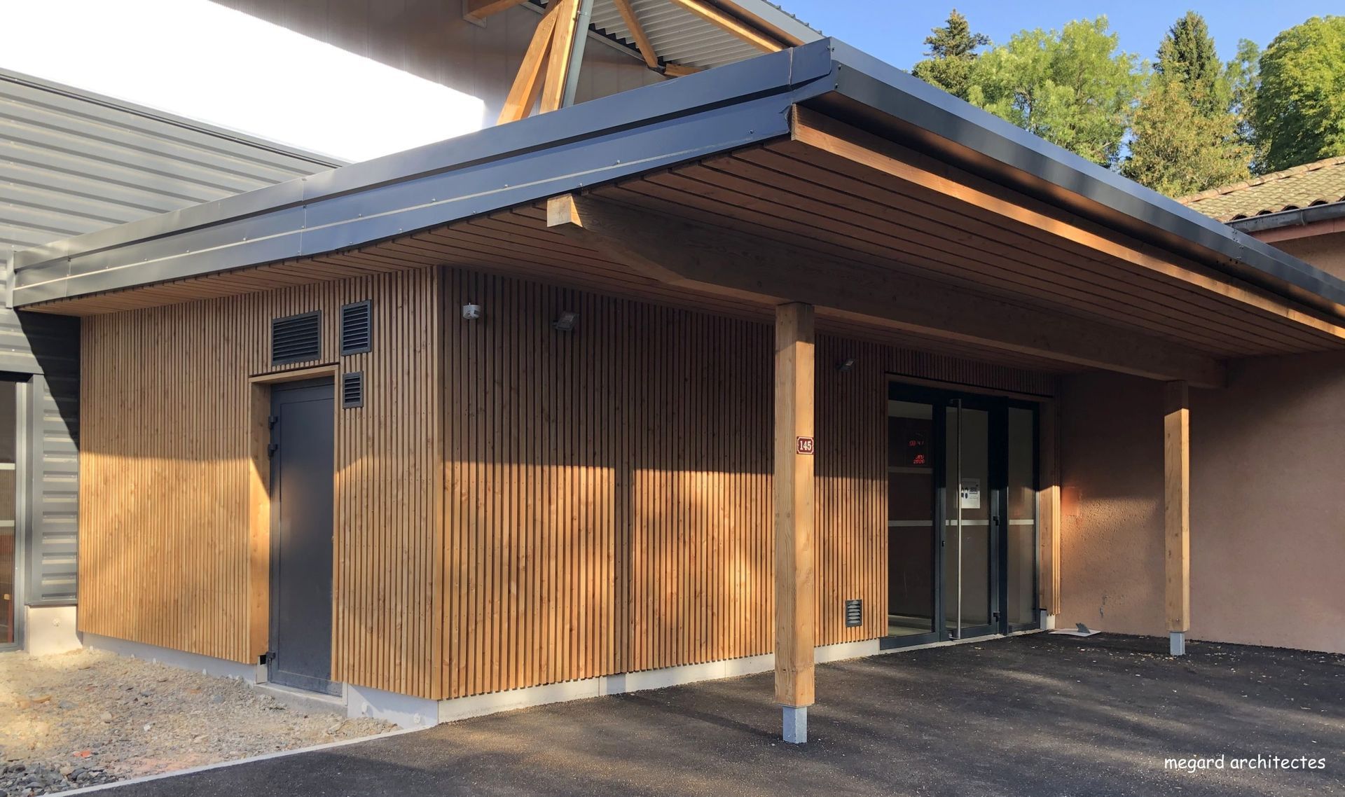 Bâtiment en bois avec un toit et un auvent sombres, à côté d'une autre construction.