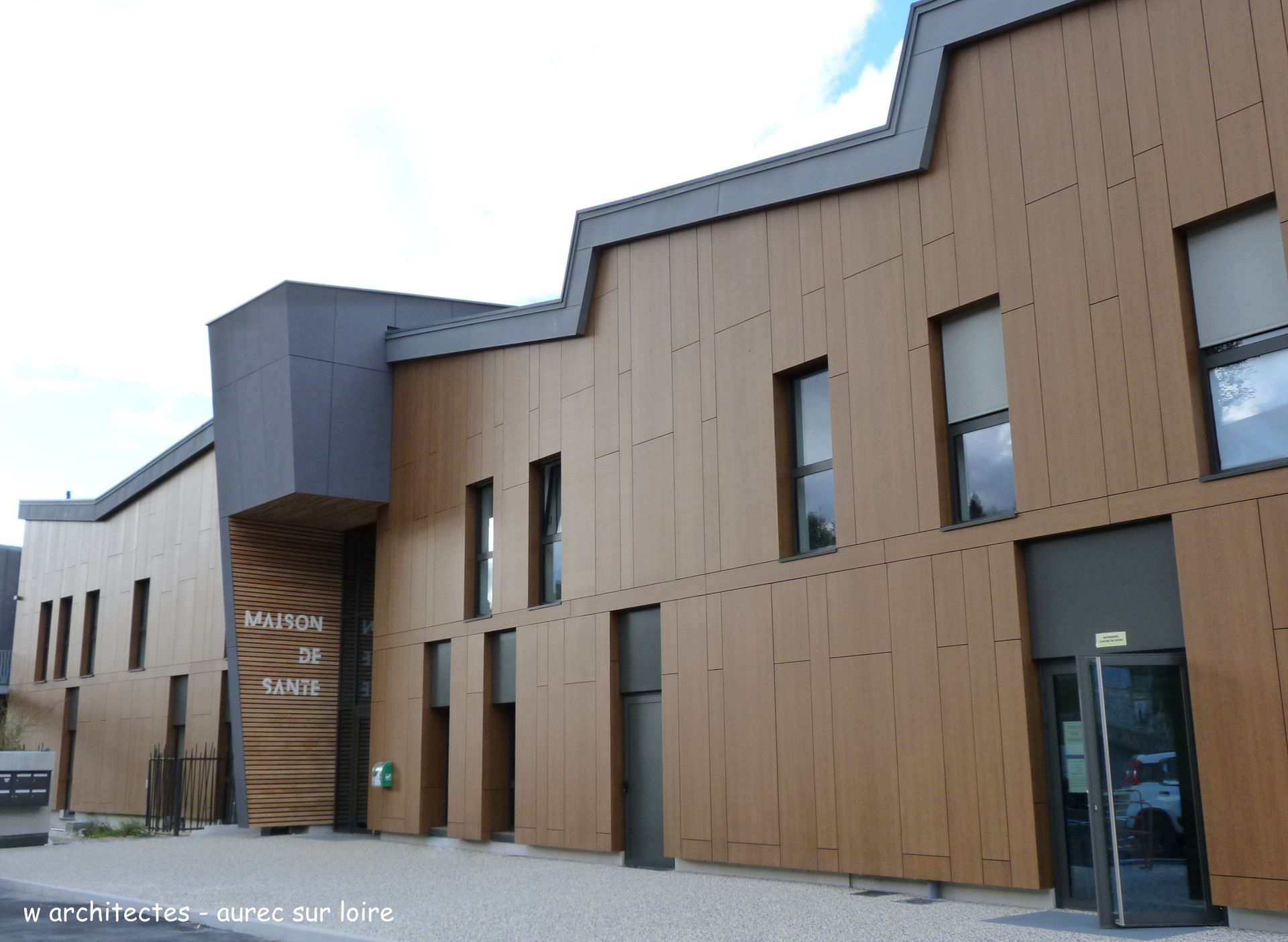 Bâtiment en bois brun avec toit angulaire, fenêtres et porte d'entrée. Enseigne « Maison de Santé ».