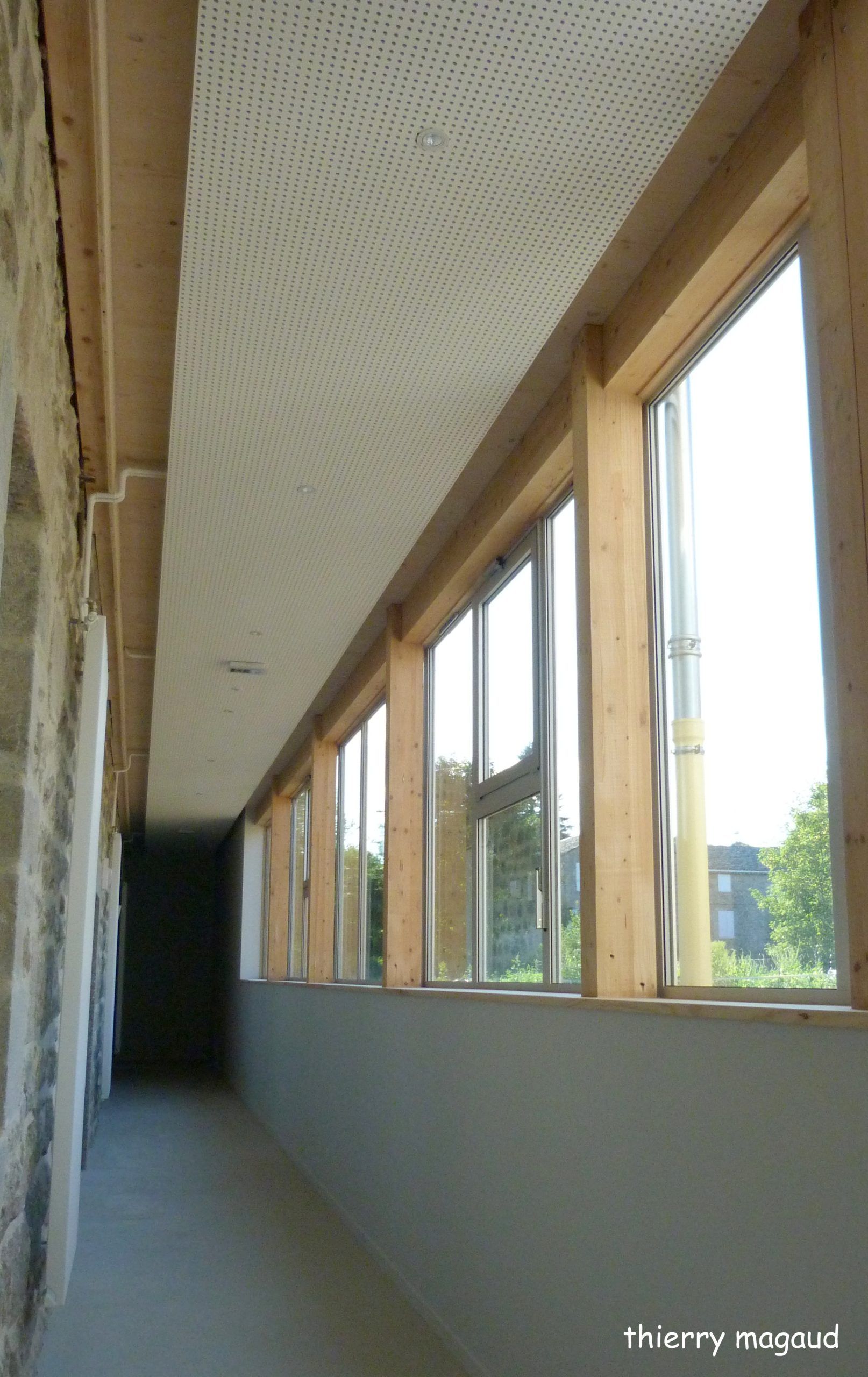 Couloir aux encadrements de fenêtres en bois, mur gris et plafond à pois. La lumière du soleil inonde la pièce.