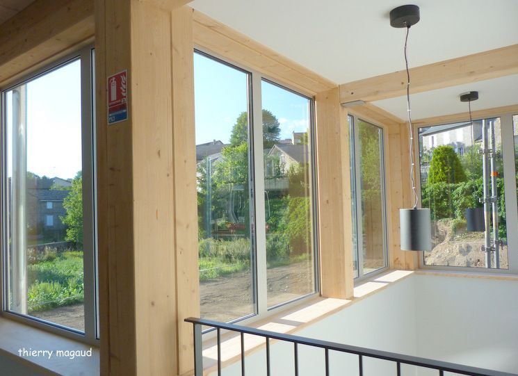 Intérieur lumineux avec de grandes fenêtres et des poutres en bois donnant sur un jardin.