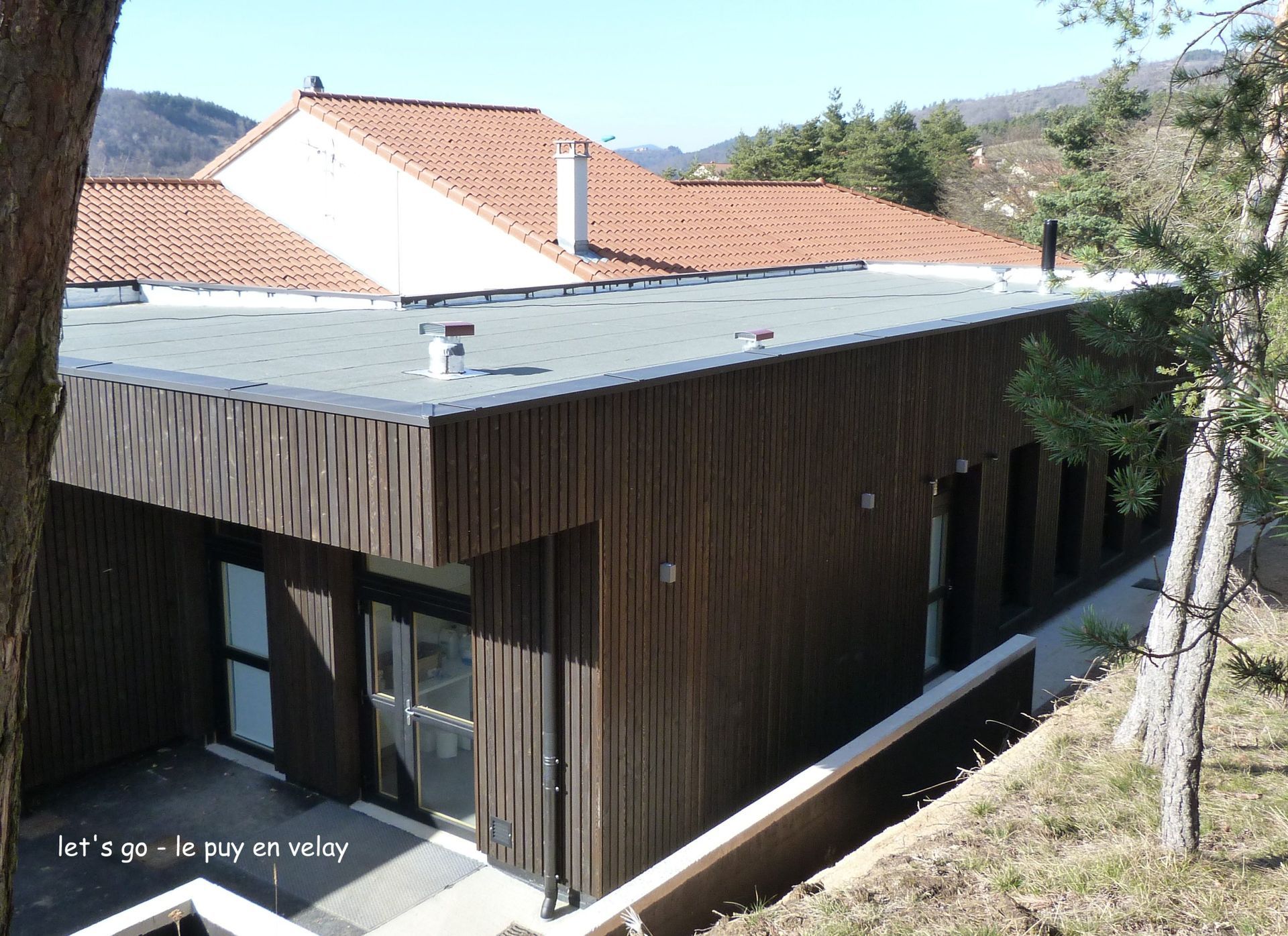 Bâtiment brun avec bardage en bois et toit de tuiles dans un paysage vallonné.