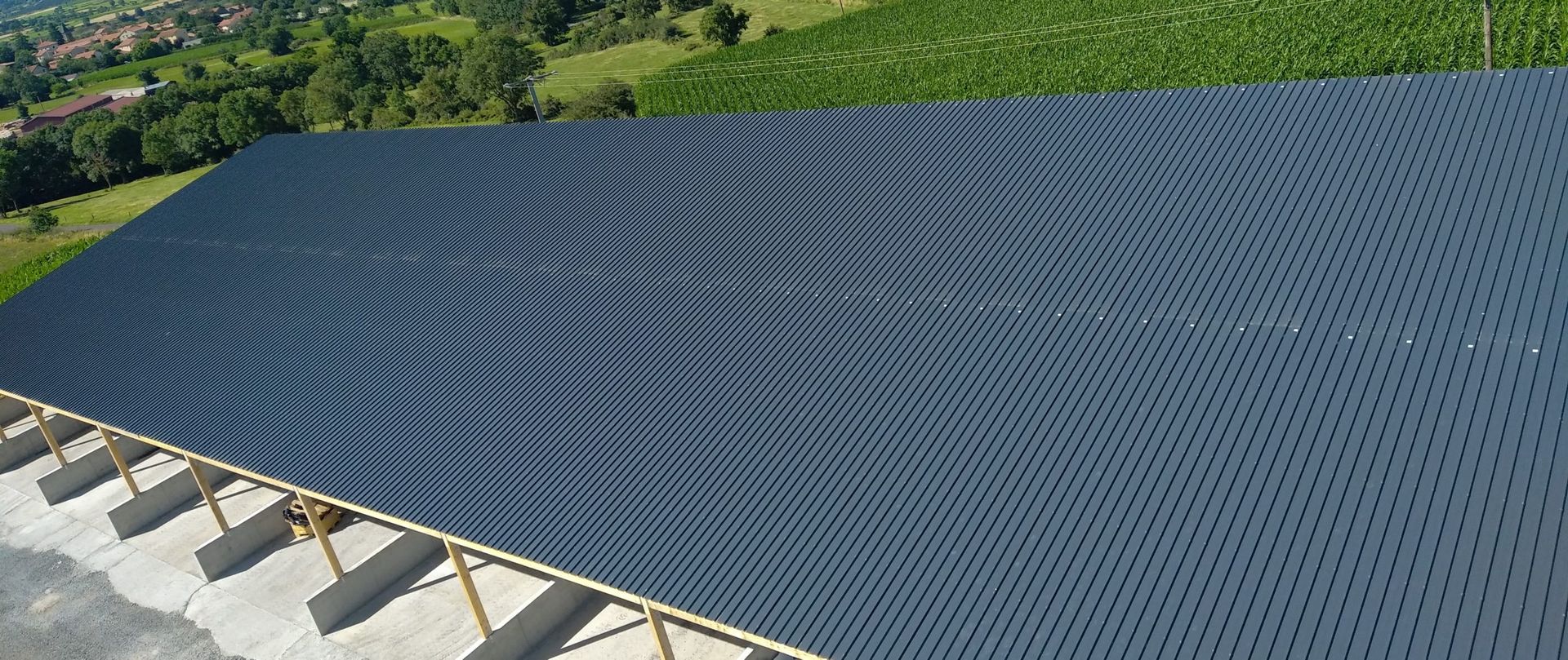 Vue aérienne d'une grande structure bleue perforée recouvrant un cadre en bois clair ; dans un champ.