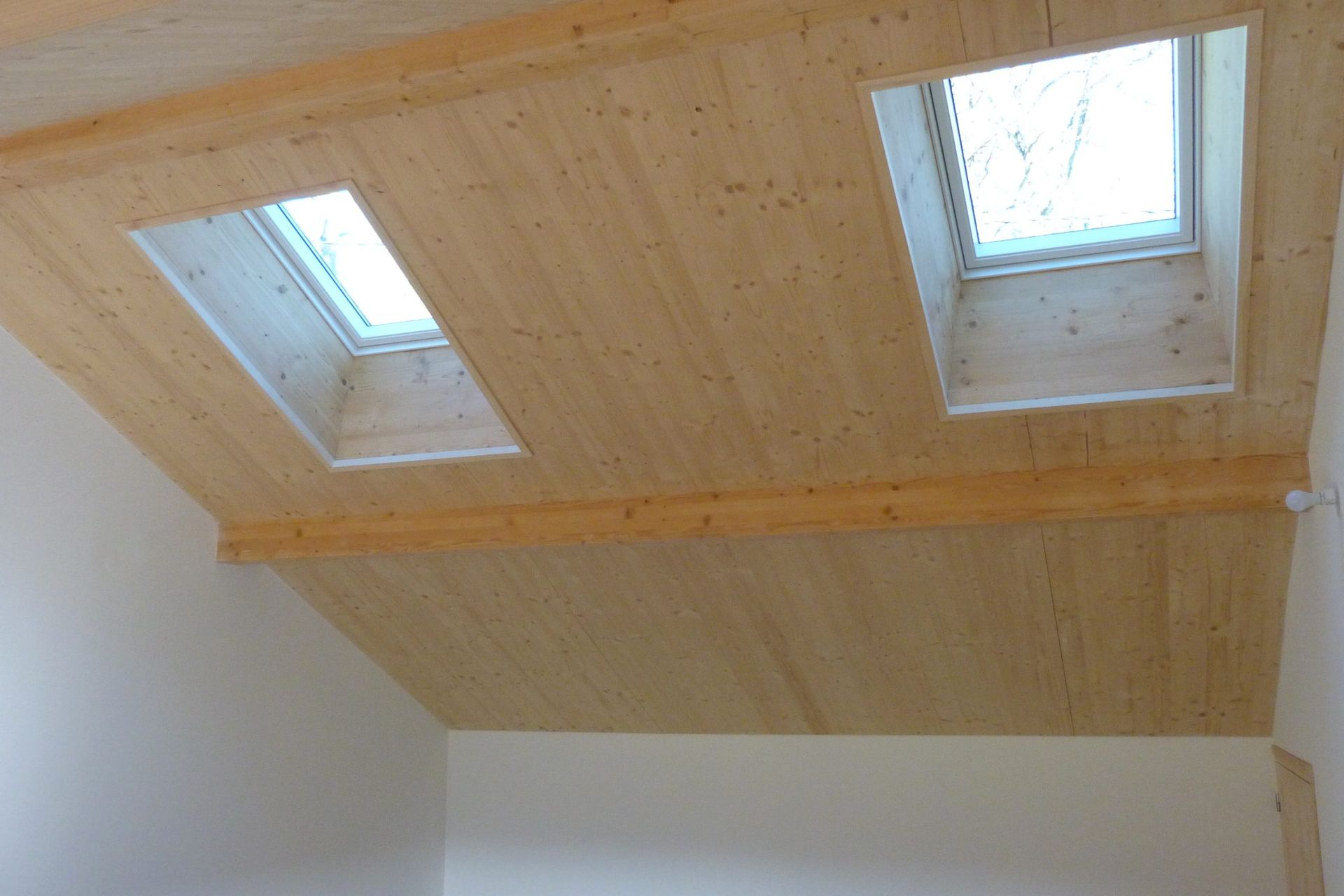 Plafond en bois avec deux puits de lumière dans une pièce aux murs blancs.
