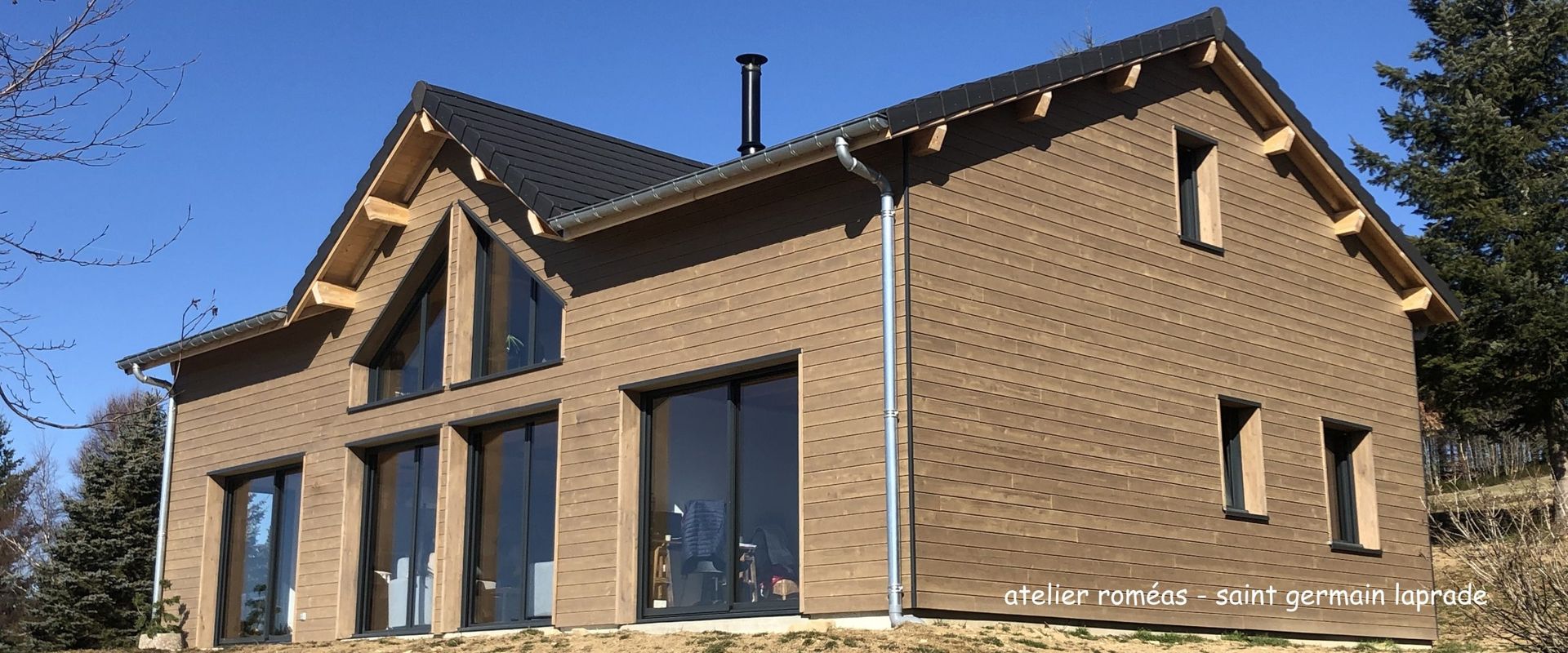 Maison en briques avec toit noir et grandes fenêtres par une journée ensoleillée.