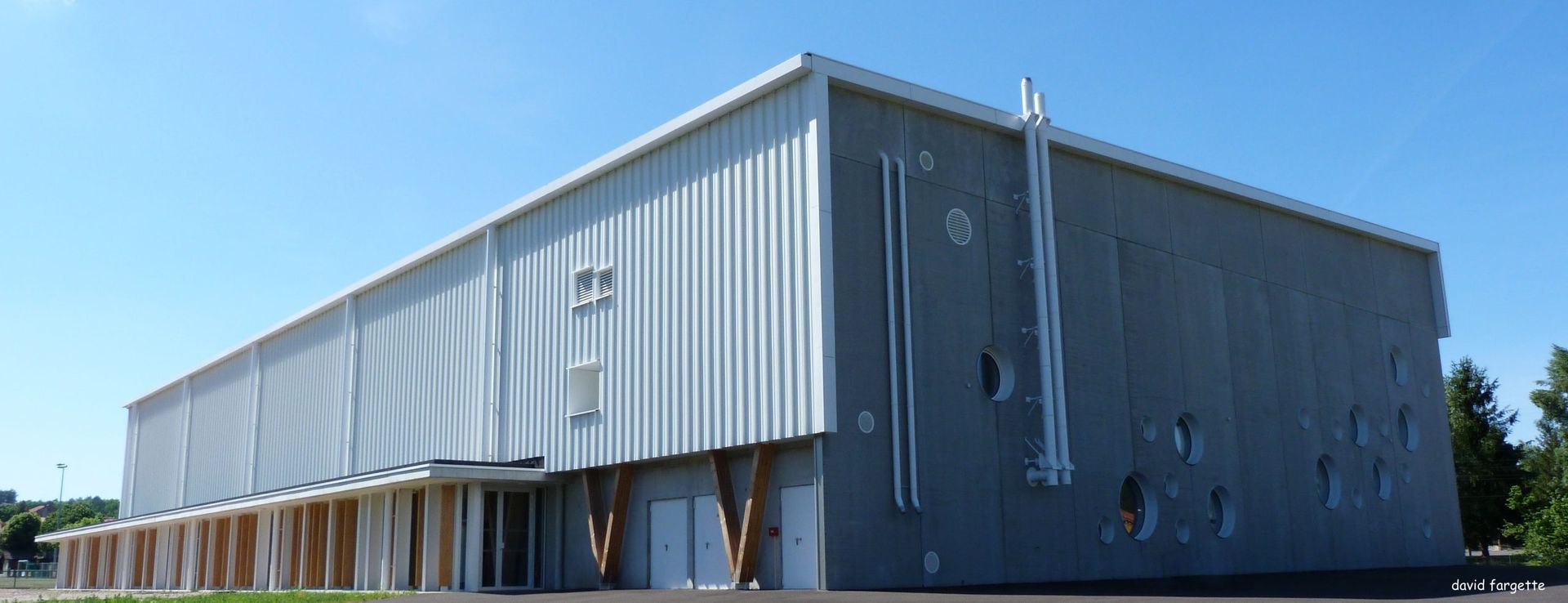 Un bâtiment moderne de style industriel, avec un bardage en tôle ondulée, un toit plat et un ciel bleu dégagé.