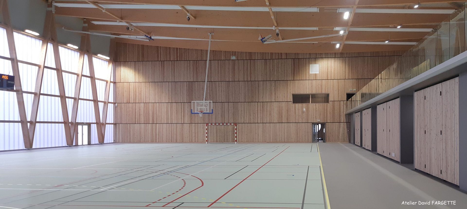 Gymnase intérieur avec murs et sol en bois, un panier de basket et de hautes fenêtres.