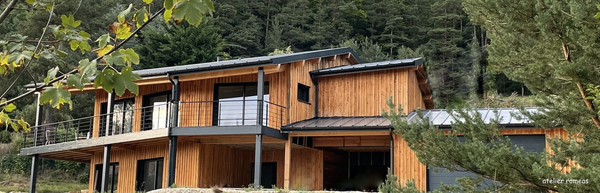 Cabane en bois aux finitions noires, entourée d'arbres verts.