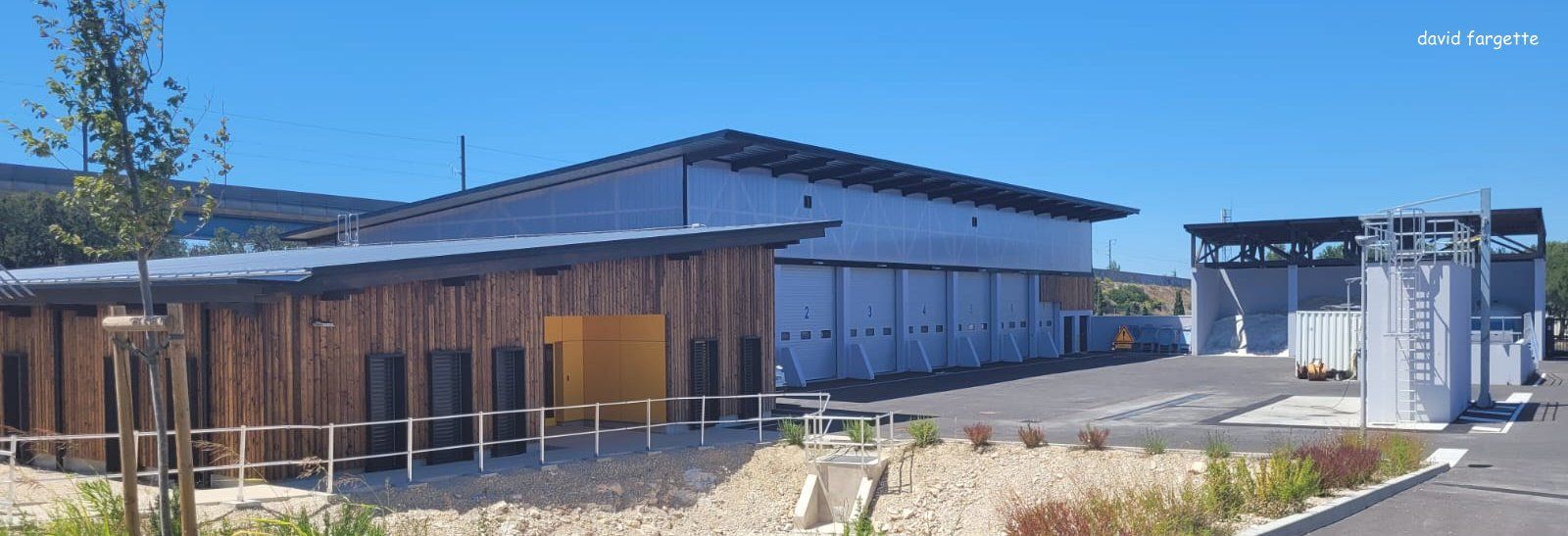 Bâtiments à façade en bois et entrepôt métallique, sous un ciel bleu.