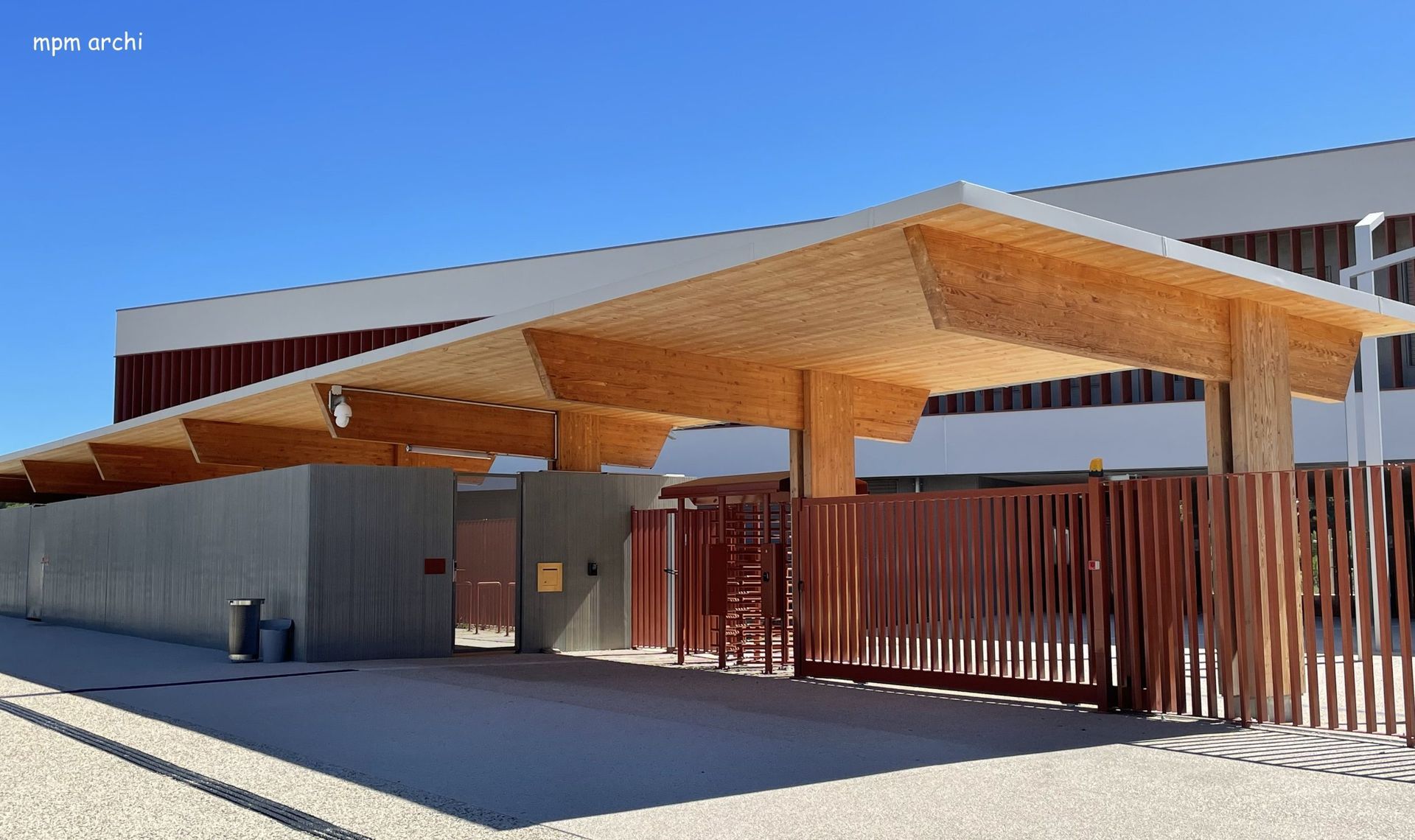 Entrée du bâtiment avec auvent en bois, clôture marron et ciel bleu clair.