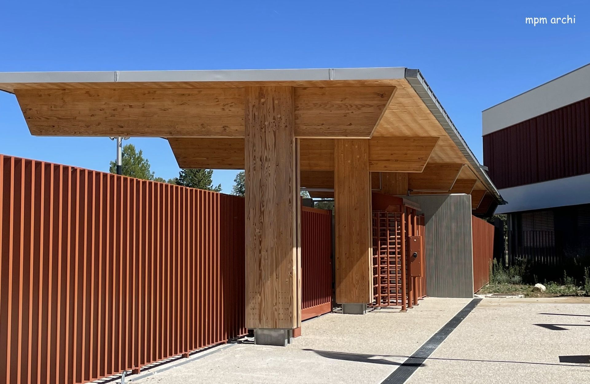 Structure en bois recouverte d'une clôture à lattes rouges ; bâtiment en arrière-plan.