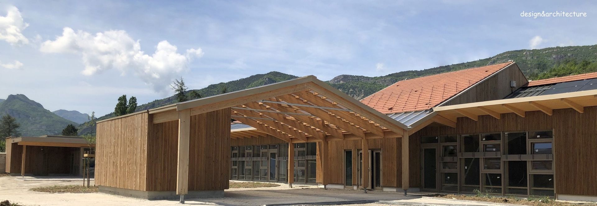 Bâtiment en bois au toit en pente, devant des montagnes et un ciel bleu.