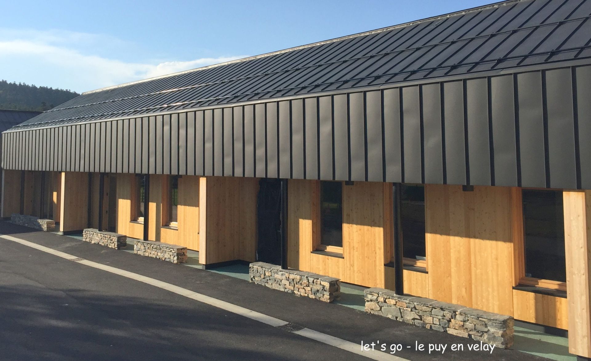 Extérieur d'un bâtiment avec un toit sombre, des murs en bois, des éléments en pierre et des fenêtres.
