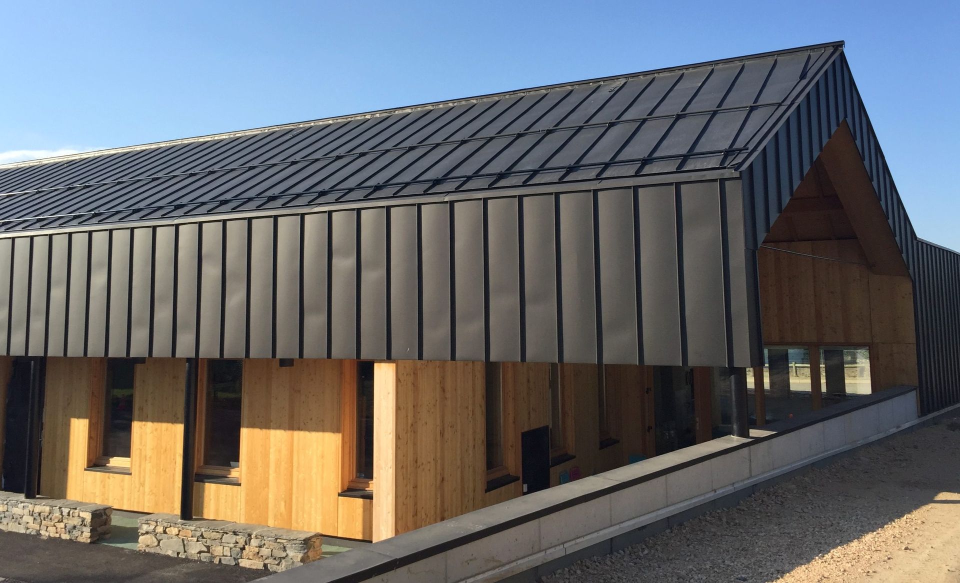 Bâtiment avec toit en métal sombre, bardage en bois et petites fenêtres. Journée ensoleillée.