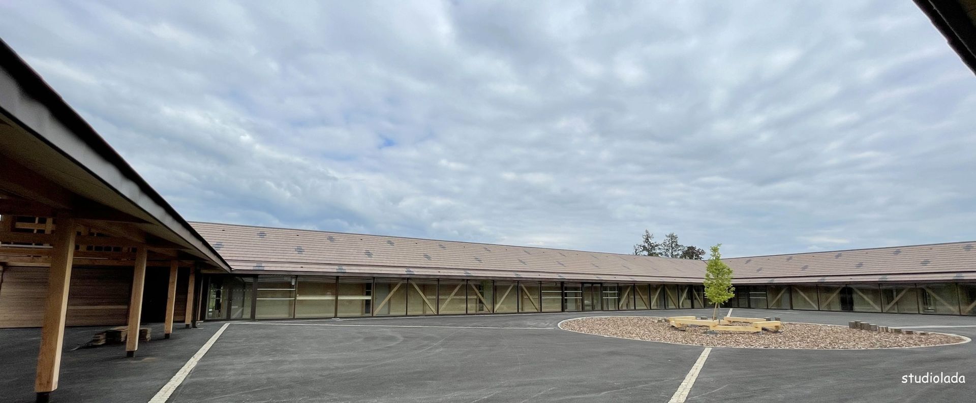 Vue extérieure d'un motel sous un ciel nuageux. Le bâtiment se compose de plusieurs chambres reliées par une allée couverte et agrémentées d'un espace vert central.